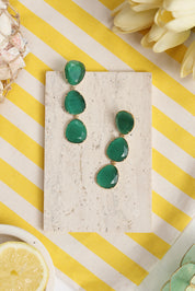 Boucles d'oreilles pendantes dorées Gisèle vert fonce ornées de pierres oeil de chat - Bijou photographié dans un décor estival