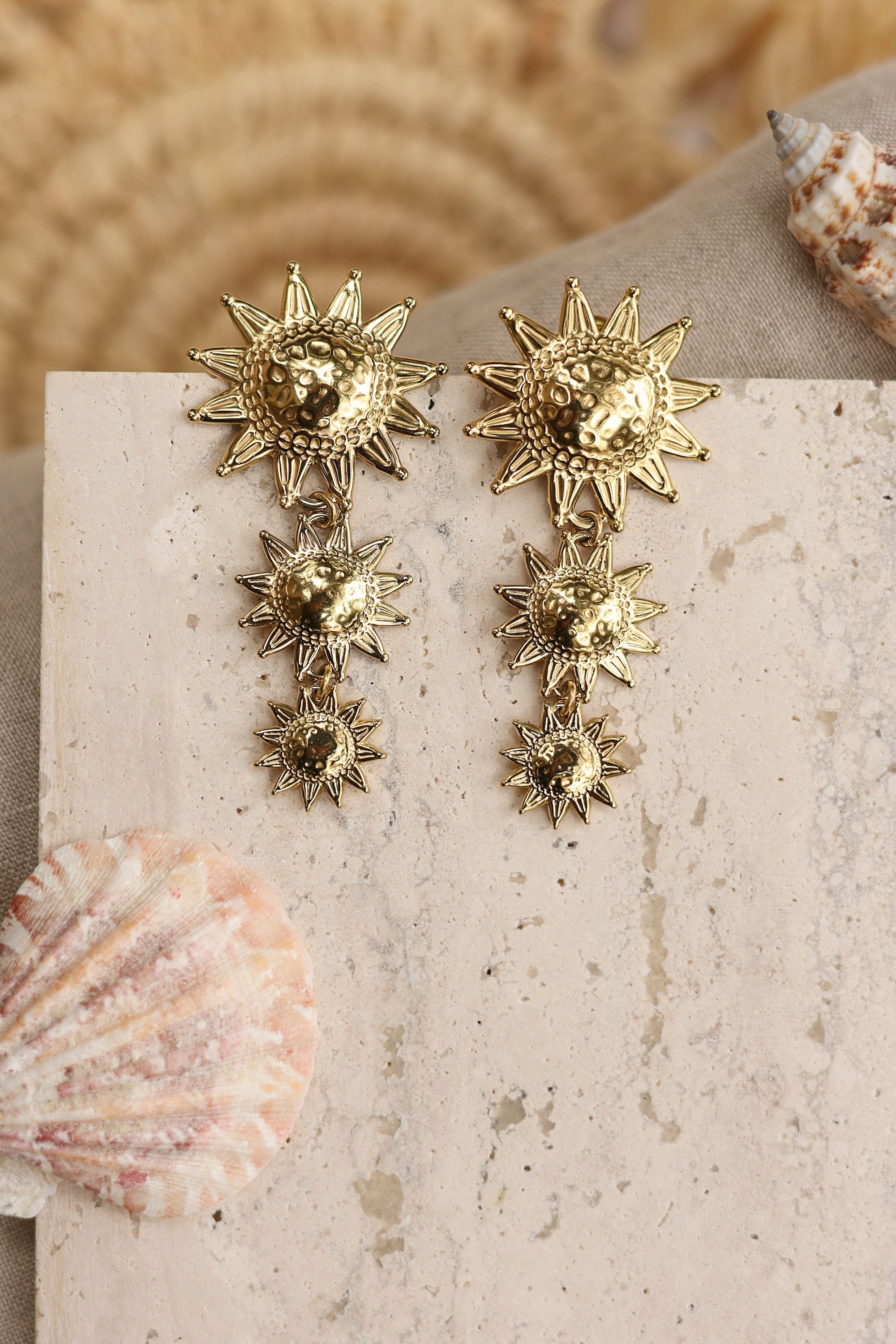 Boucles d'oreilles pendantes dorées Michaela soleils - Bijou photographié dans un décor estival