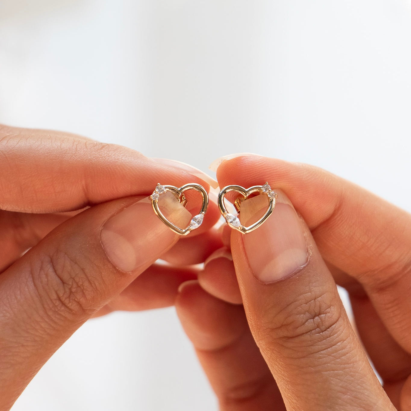 Boucles d’oreilles Galinda dorées cœurs zircons - Bijou photographié dans les mains 