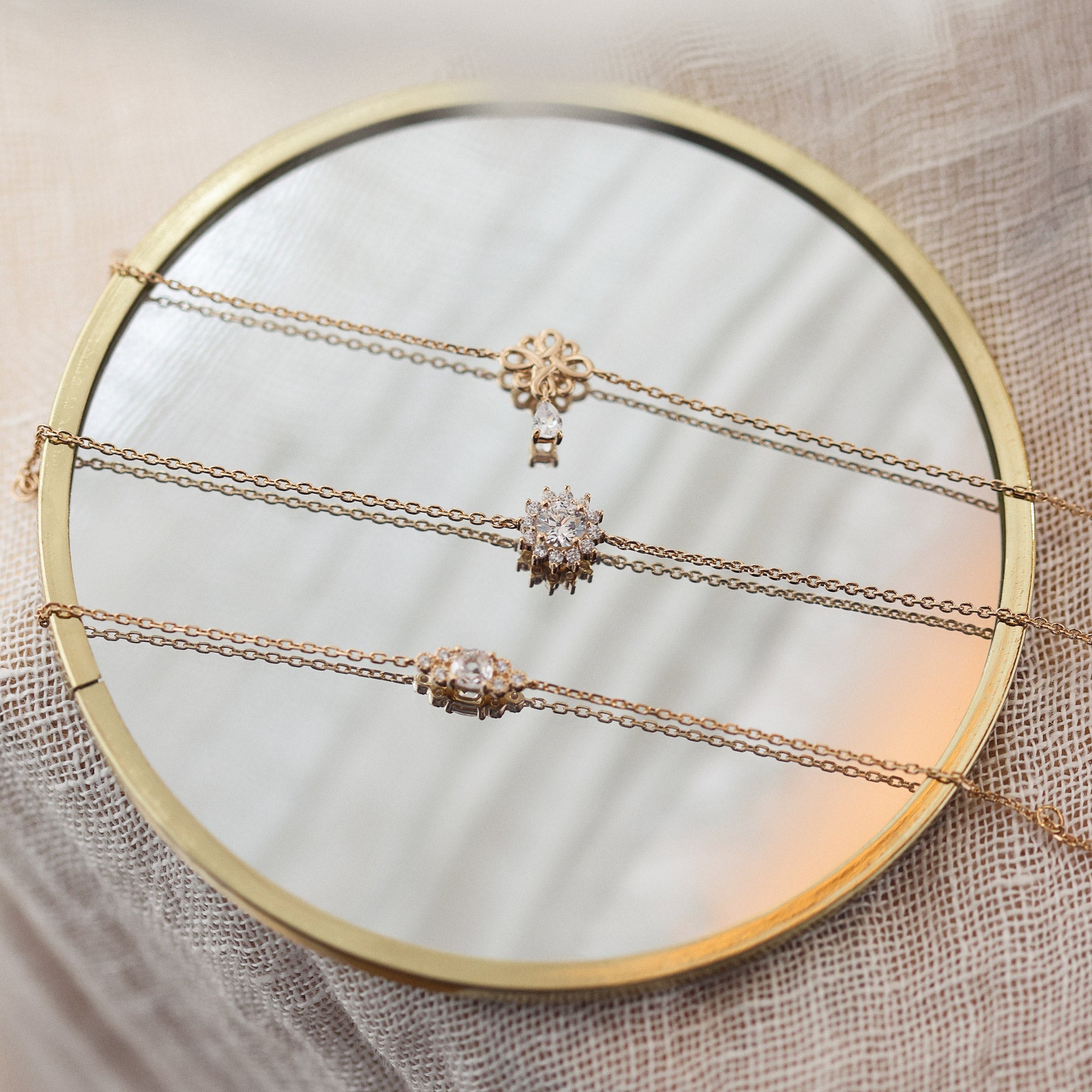 Bracelet doré Joanie avec un pendentif nœud de l’infini et un zircon en forme de goutte suspendu - Bijou photographié sur un miroir rond 