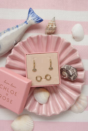 Coffret de parure de bijoux Beam comprenant une paire de mini créoles dorées ornées d’un œil serti d'un zircon ainsi qu’une paire de créoles simples - Bijoux photographiés dans un décor estival