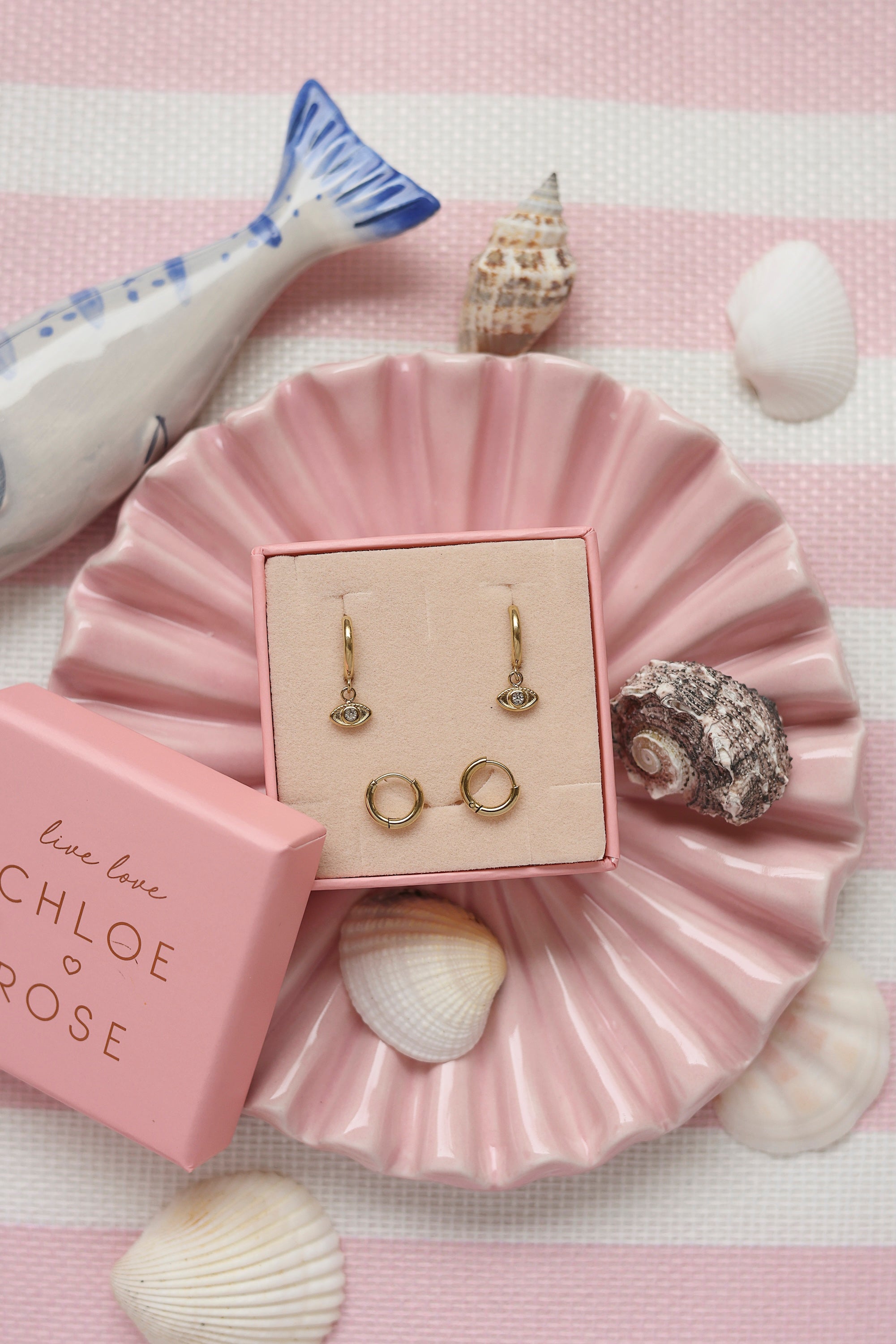 Coffret de parure de bijoux Beam comprenant une paire de mini créoles dorées ornées d’un œil serti d'un zircon ainsi qu’une paire de créoles simples - Bijoux photographiés dans un décor estival