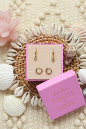 Coffret de parure de bijoux Kelia comprenant une paire de mini créoles dorées ornées d’un cœur ainsi qu’une paire de créoles simples - Bijoux photographiés dans un décor estival