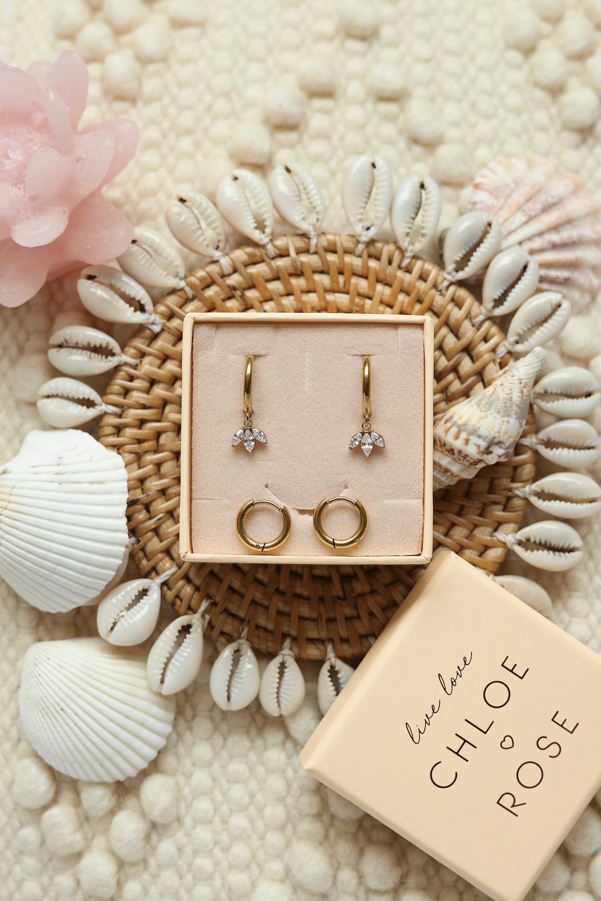 Coffret de parure de bijoux Mirage comprenant une paire de mini créoles dorées ornées d’un pendentif pétales serti de zircons ainsi qu’une paire de créoles simples - Bijoux photographiés dans un décor estival