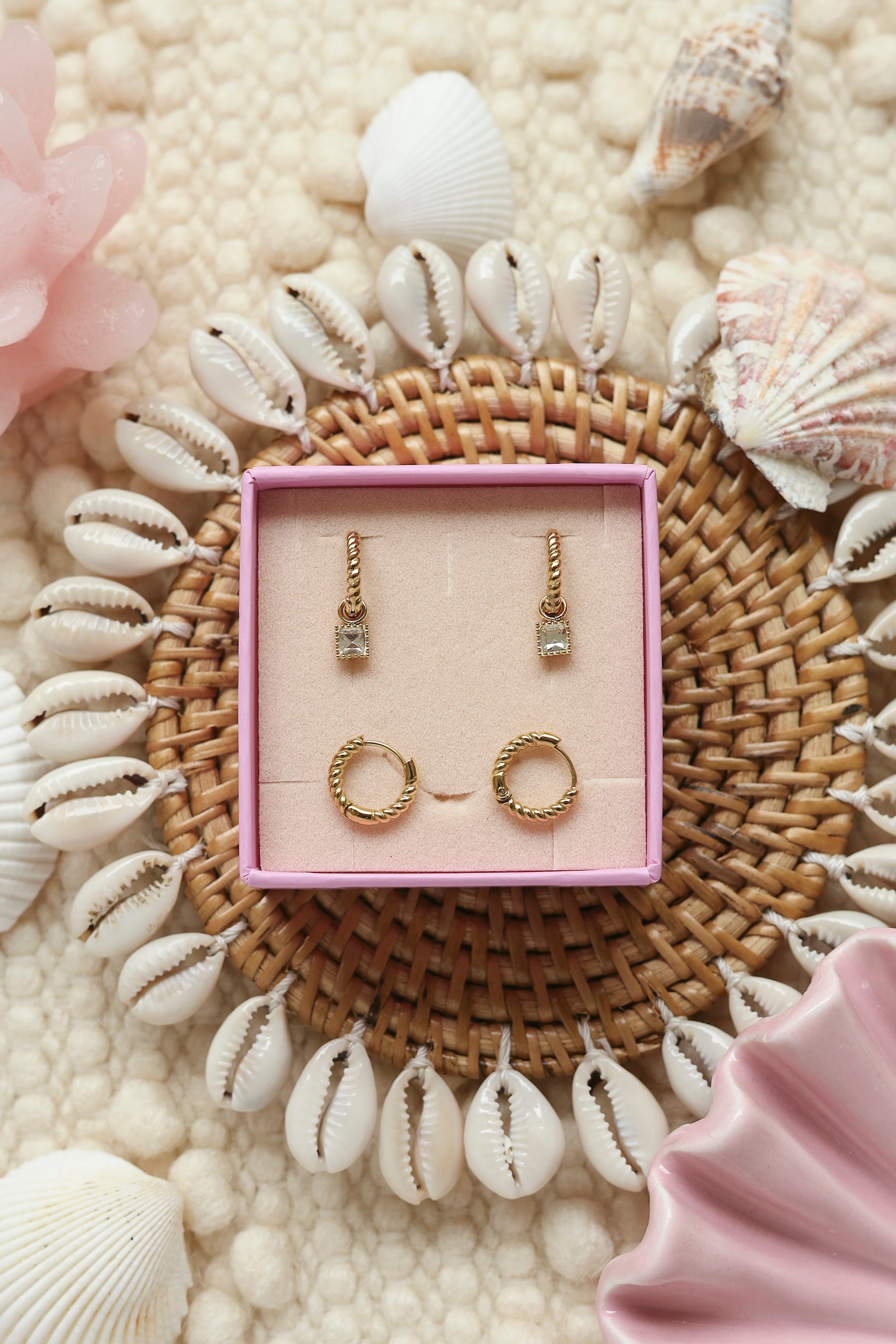 Coffret de parure de bijoux Lush blanc comprenant une paire de mini créoles torsadées dorées ornées d’un zircon carré blanc ainsi qu’une paire de créoles torsadées simples - Bijoux photographiés dans un décor estival