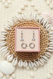 Coffret de parure de bijoux Mirage comprenant une paire de mini créoles argentées ornées d’un pendentif pétales serti de zircons ainsi qu’une paire de créoles simples - Bijoux photographiés dans un décor estival
