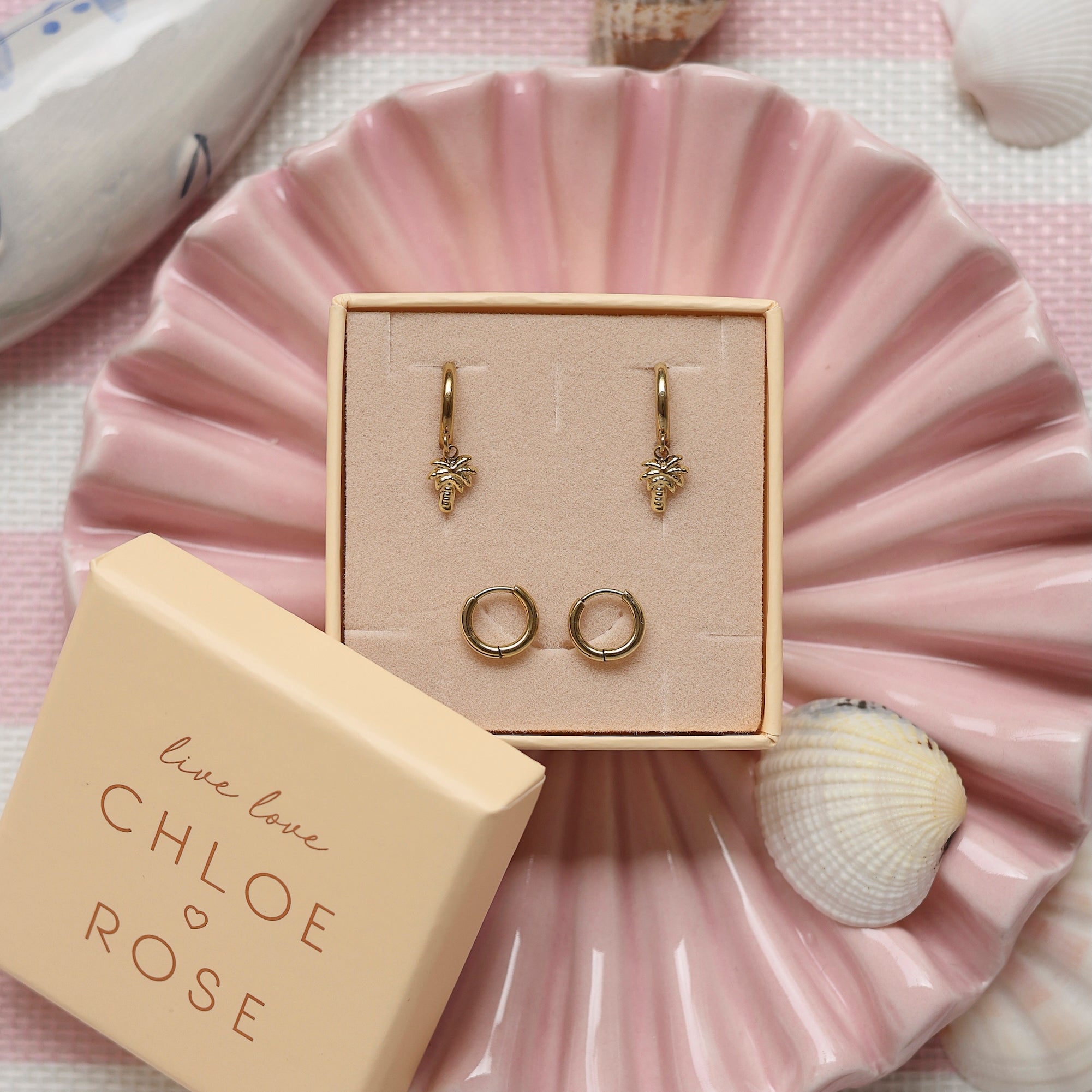 Coffret de parure de bijoux Palmier comprenant une paire de mini créoles dorées ornées d’un palmier ainsi qu’une paire de créoles simples - Bijoux photographiés dans un décor estival
