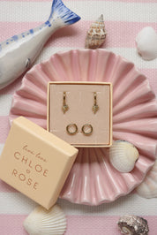 Coffret de parure de bijoux Palmier comprenant une paire de mini créoles dorées ornées d’un palmier ainsi qu’une paire de créoles simples - Bijoux photographiés dans un décor estival
