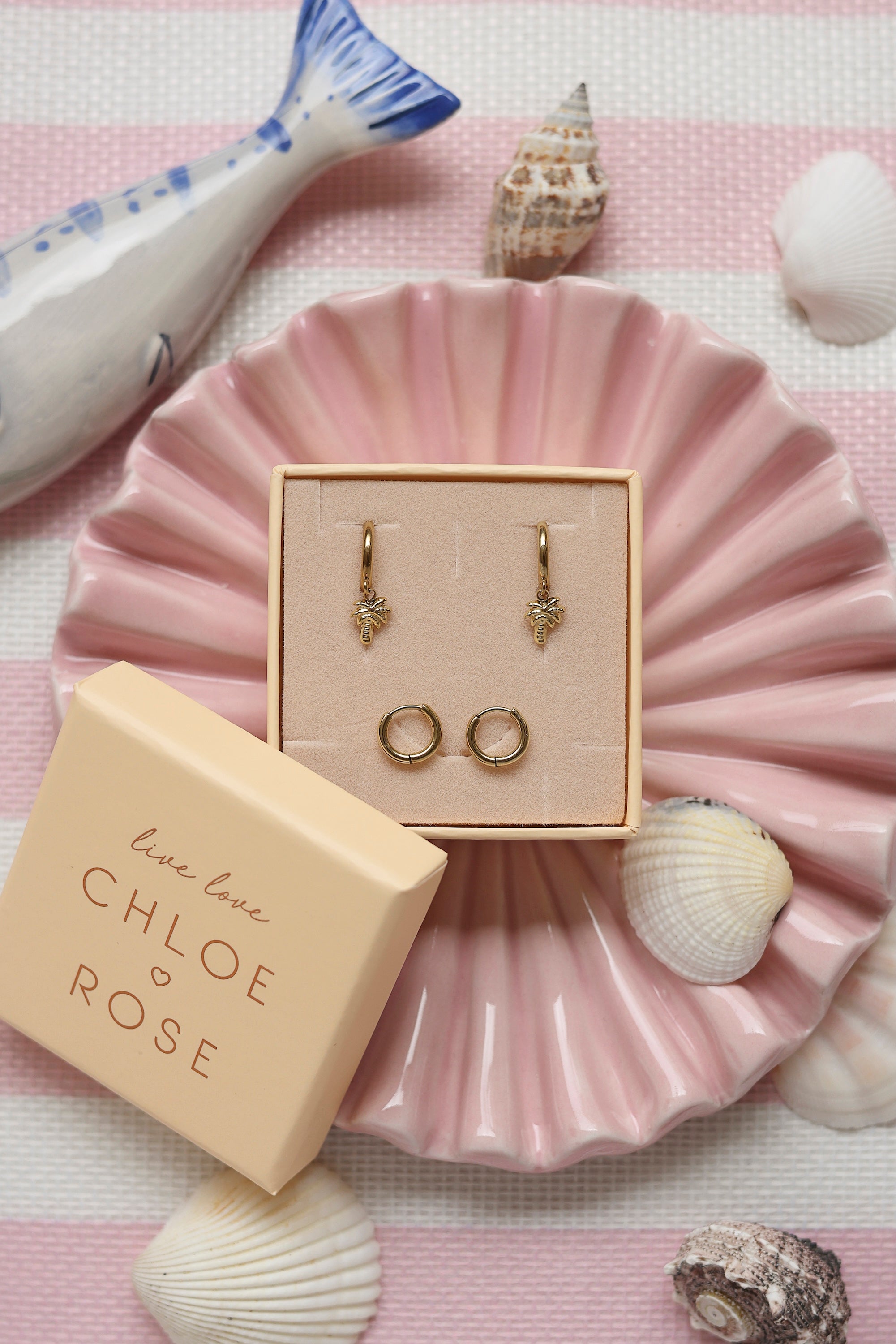 Coffret de parure de bijoux Palmier comprenant une paire de mini créoles dorées ornées d’un palmier ainsi qu’une paire de créoles simples - Bijoux photographiés dans un décor estival
