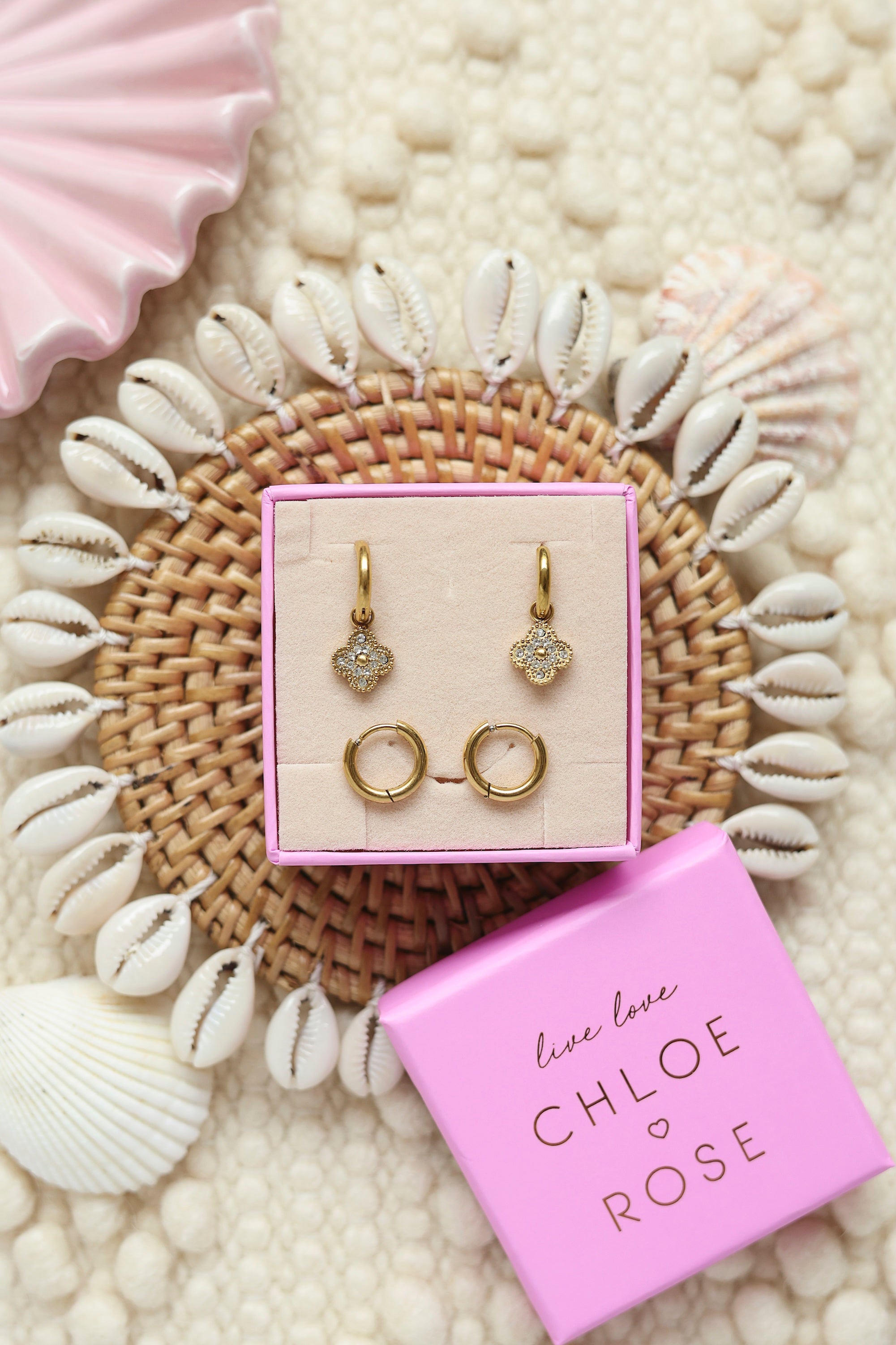 Coffret de parure de bijoux Shore comprenant une paire de mini créoles dorées ornées d’une fleur sertie de zircons ainsi qu’une paire de créoles simples - Bijoux photographiés dans un décor estival
