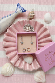 Coffret de parure de bijoux Starfish comprenant une paire de mini créoles argentées ornées d’une étoile de mer ainsi qu’une paire de créoles simples - Bijoux photographiés dans un décor estival
