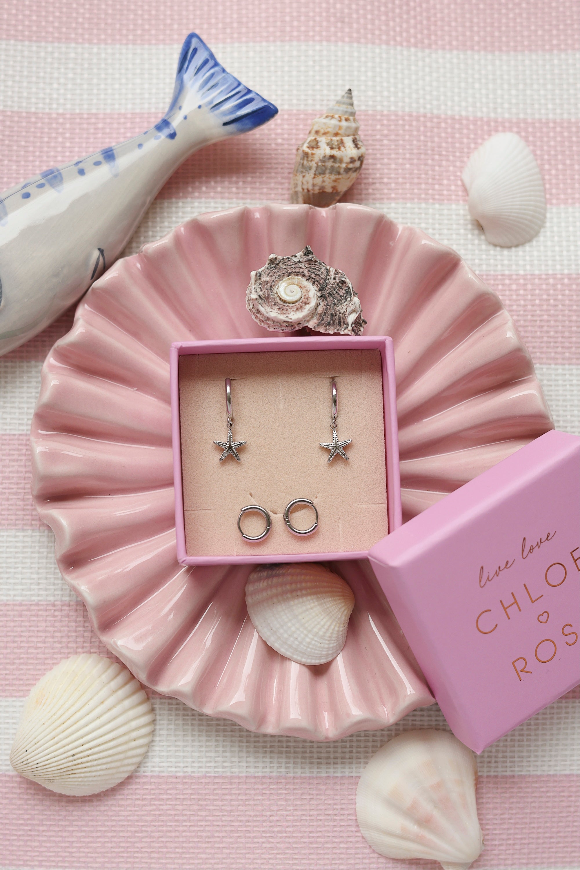 Coffret de parure de bijoux Starfish comprenant une paire de mini créoles argentées ornées d’une étoile de mer ainsi qu’une paire de créoles simples - Bijoux photographiés dans un décor estival