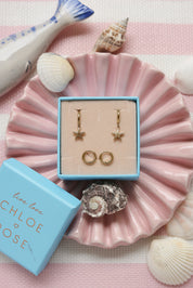 Coffret de parure de bijoux Starfish comprenant une paire de mini créoles dorées ornées d’une étoile de mer ainsi qu’une paire de créoles simples - Bijoux photographiés dans un décor estival