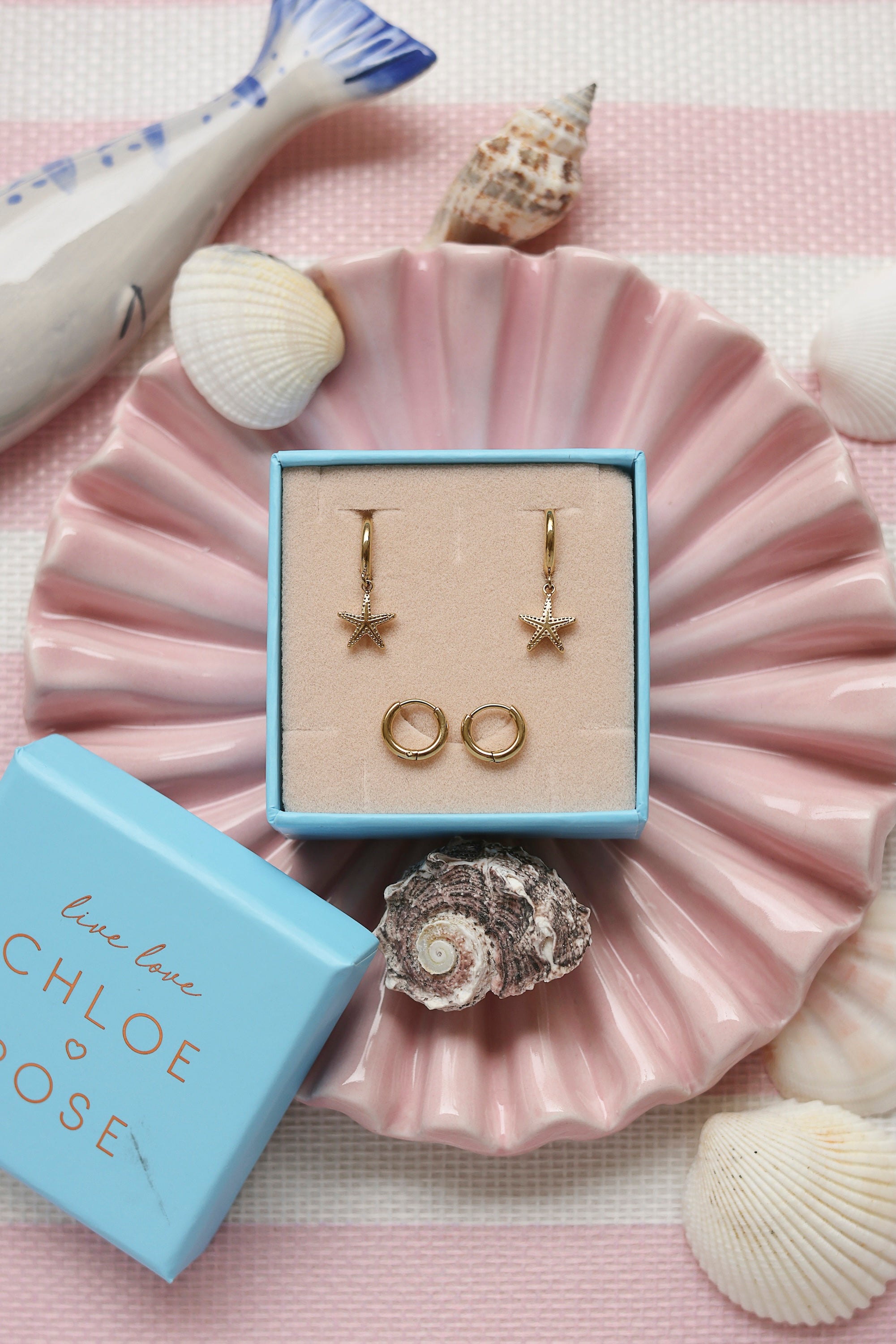 Coffret de parure de bijoux Starfish comprenant une paire de mini créoles dorées ornées d’une étoile de mer ainsi qu’une paire de créoles simples - Bijoux photographiés dans un décor estival