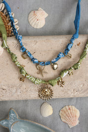 Collier doré Yarina bleu tissu bandana bleu avec pendentifs étoile de mer et coquillages - Bijou photographié dans un décor estival