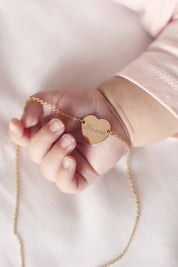Collier personnalisable doré Adelie chaîne fine et médaille en forme de cœur à graver - Bijou porté dans une main de bébé