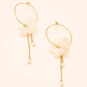 Boucles d'oreilles créoles dorées Oly L avec fleur en nacre et chaînes pendantes - Bijou photographié sur fond beige
