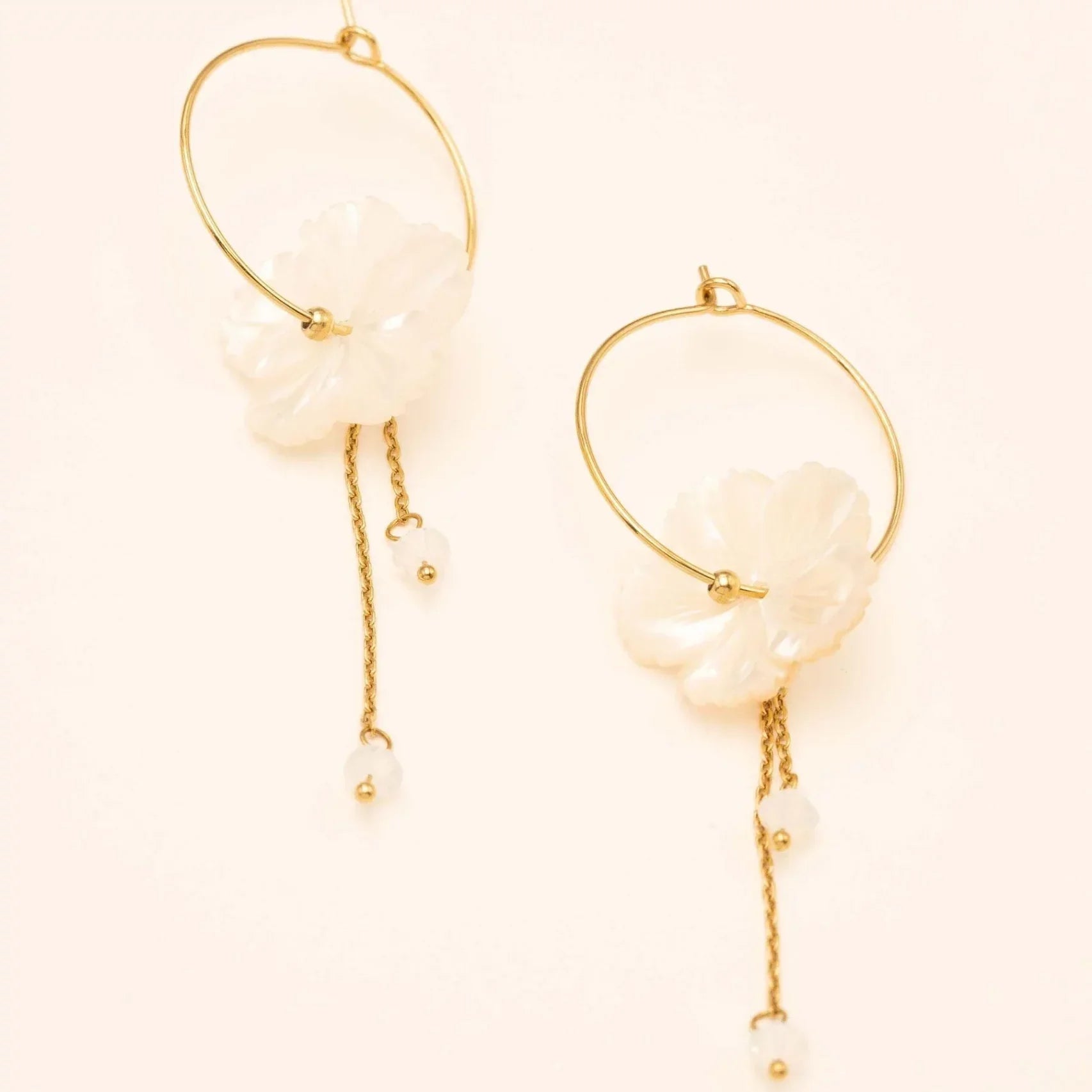 Boucles d'oreilles créoles dorées Oly L avec fleur en nacre et chaînes pendantes - Bijou photographié sur fond beige