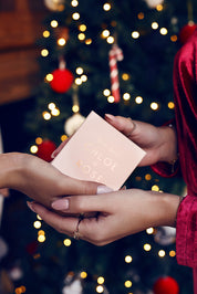 Deux mains de femmes qui se joignent en se donnant une boîte cadeau Chloé Rose dans une ambiance de Noël