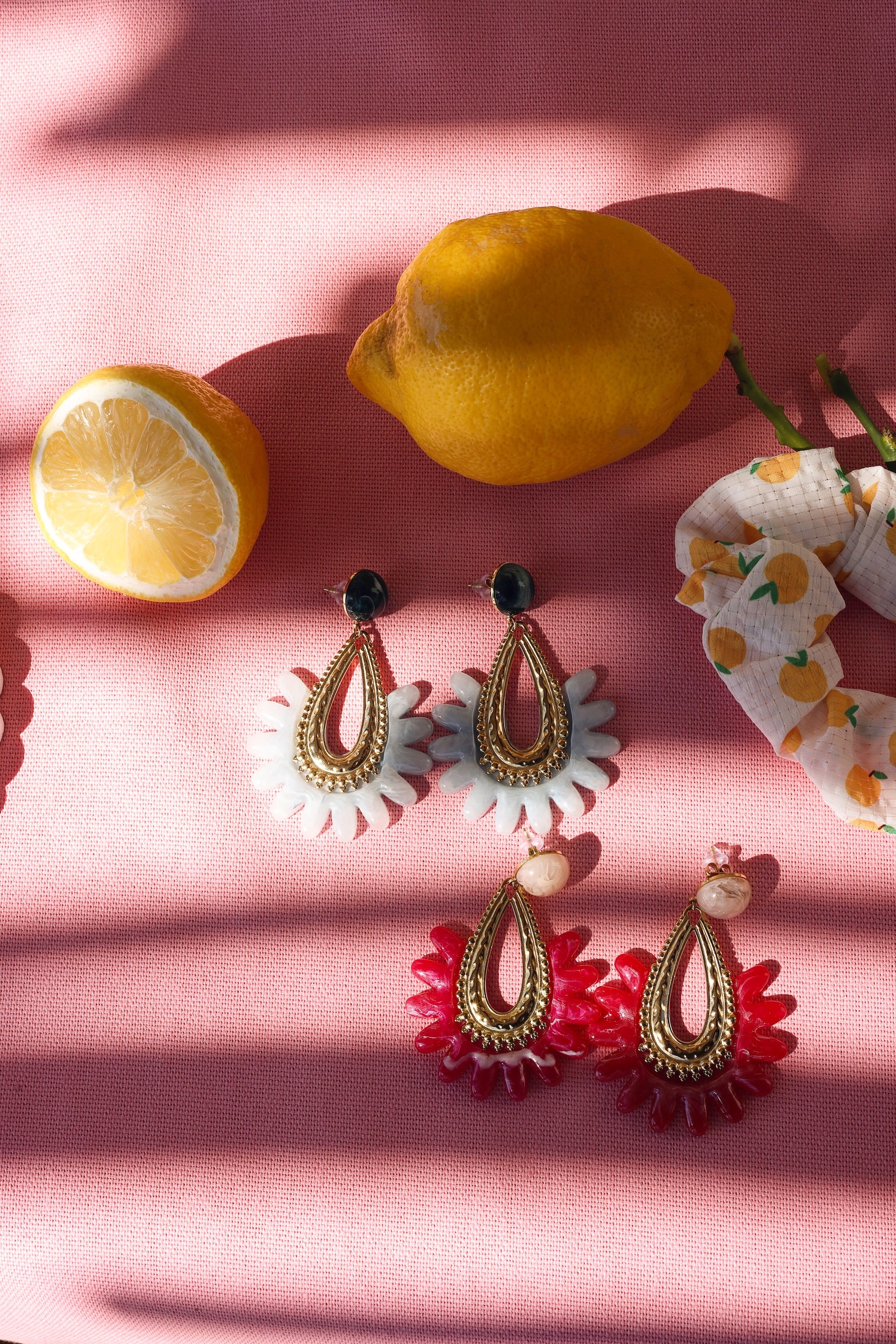 Boucles d'oreilles pendantes Letizia rose en acétate et acier inoxydable doré - Bijou photographié sur tissu rose avec citrons