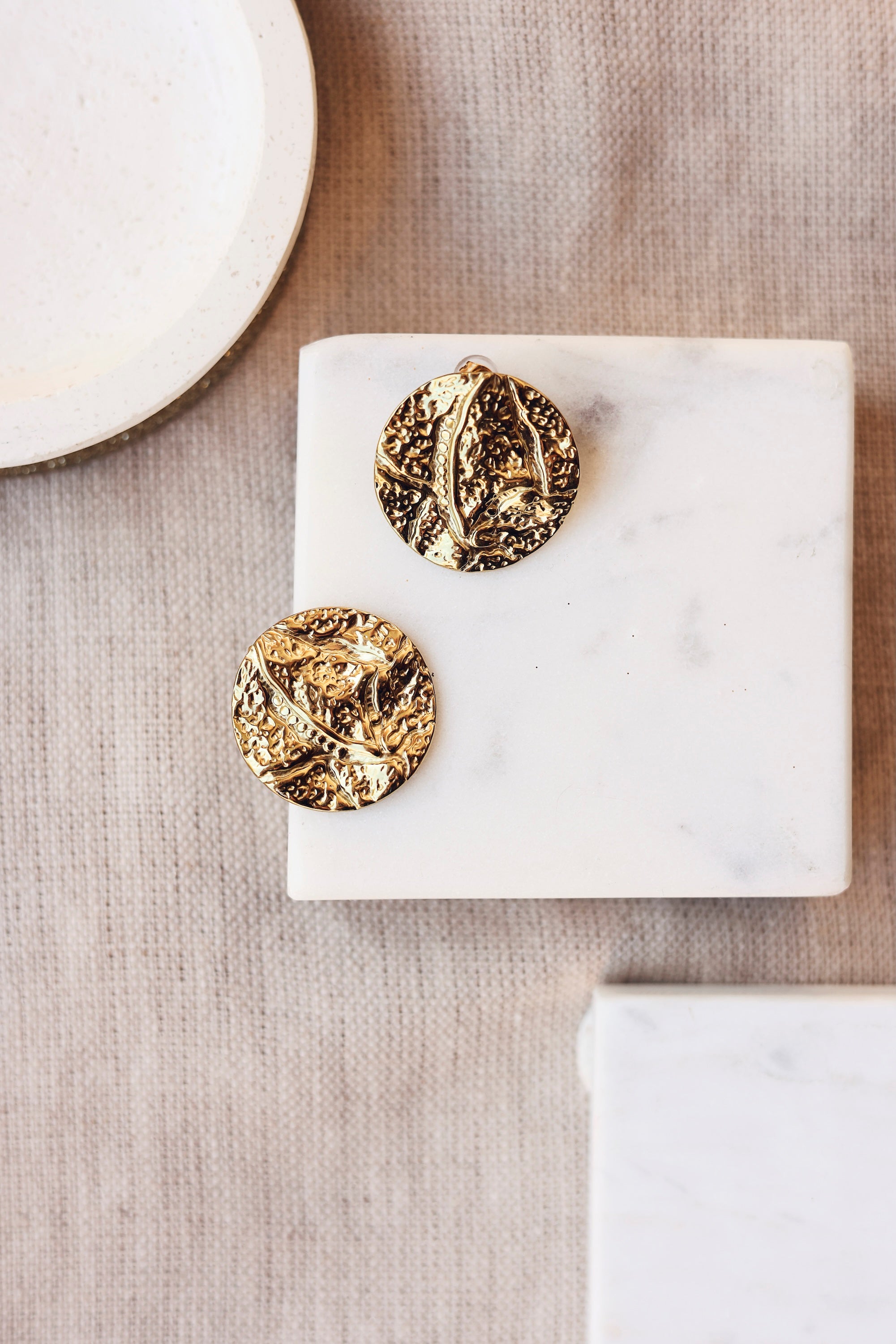 Boucles d'oreilles clous dorées Loana rondes martelée - Bijou photographié sur un présentoir en marbre blanc