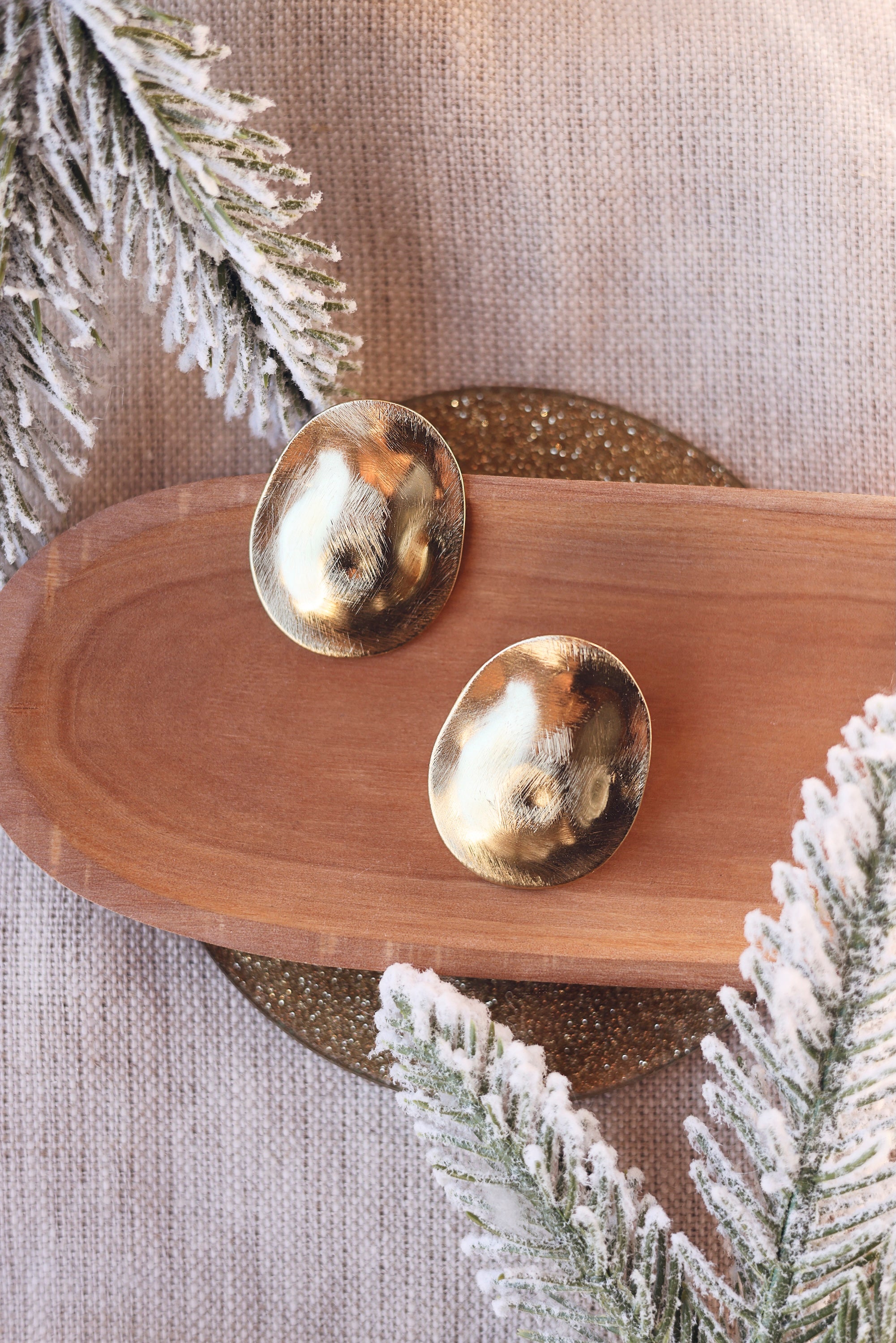 Boucles d'oreilles clous dorées Terenza ovales brossées - Bijou photographié dans une coupole en bois avec des branches de sapin