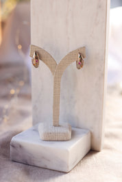 Boucles d'oreilles créoles dorées Janina striées et ornées de zircons colorés - Bijou photographié sur un présentoir en lin