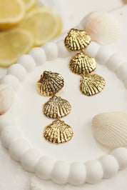 Boucles d'oreilles pendantes dorées Gillian coquillages - Bijou photographié dans un décor estival