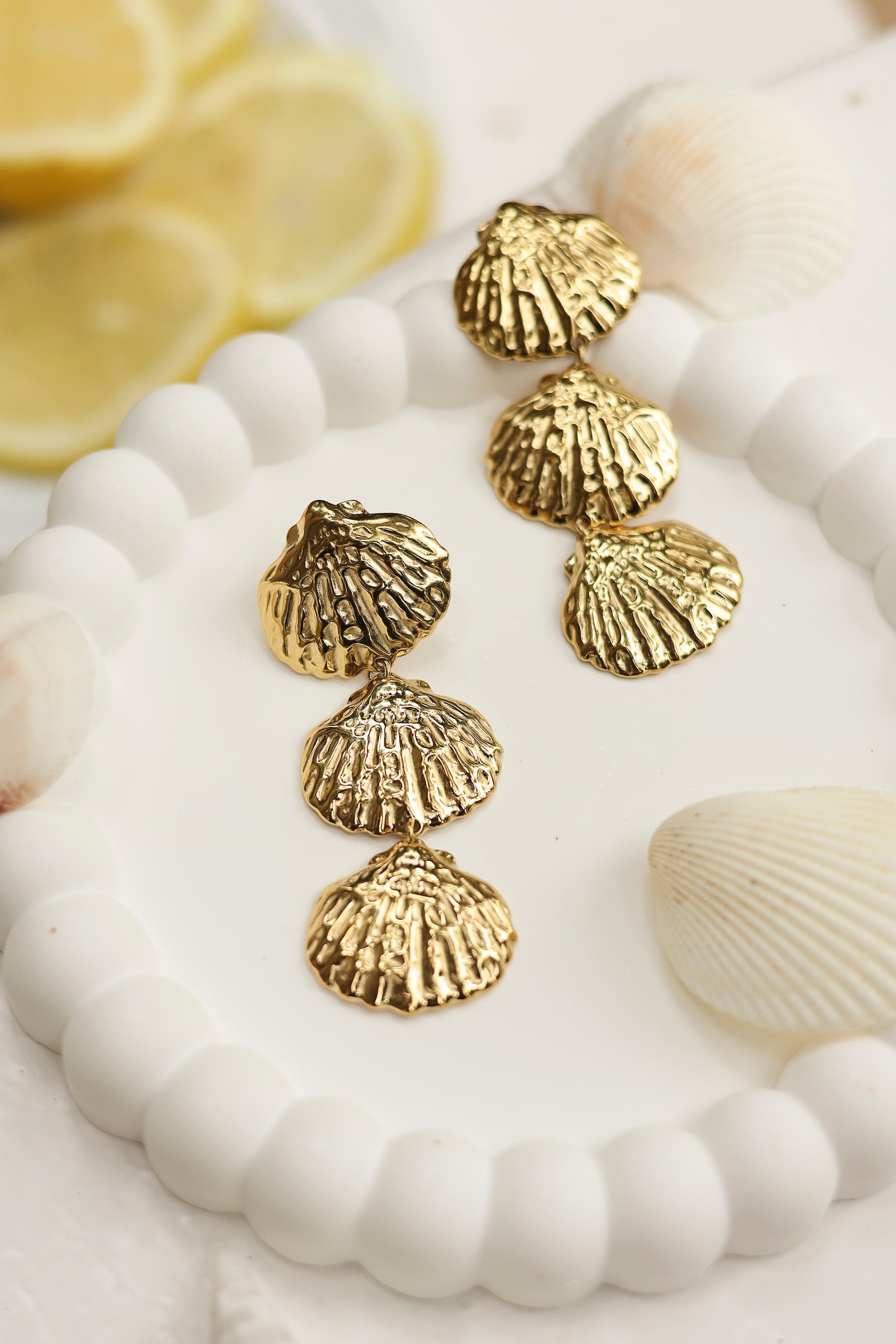 Boucles d'oreilles pendantes dorées Gillian coquillages - Bijou photographié dans un décor estival