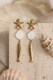 Boucles d'oreilles pendantes dorées Kiera étoile de mer, poisson et coquillage en nacre - Bijou photographié dans un décor estival