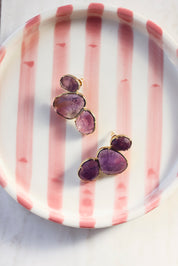 Boucles d'oreilles clous Lindsay améthyste dorées ornées de pierres naturelles - Bijou photographié dans un vide poche rose et blanc
