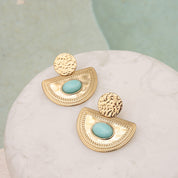 Boucles d'oreilles pendantes dorées Solal amazonite - Bijou photographié sur un présentoir en marbre blanc à côté d'une piscine