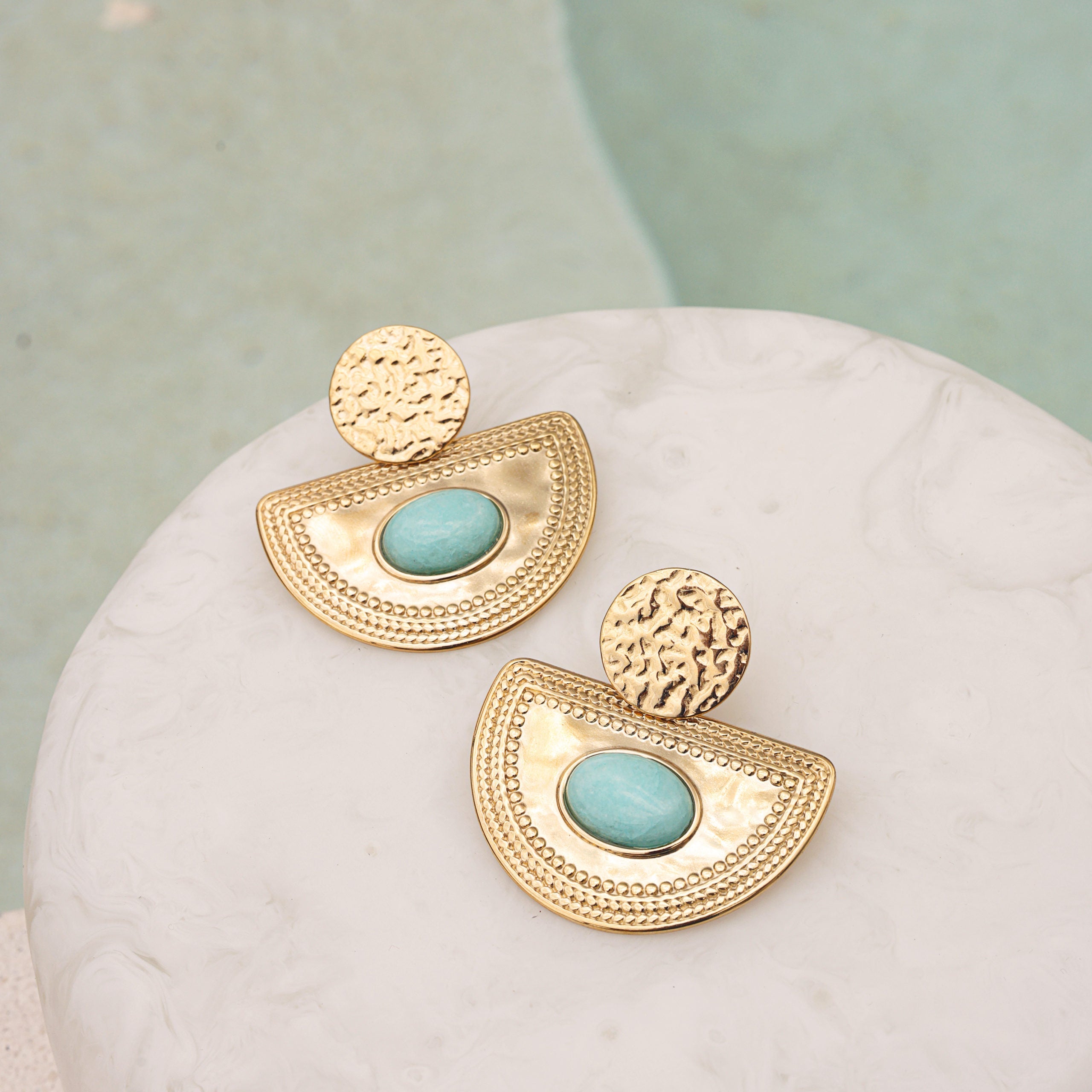 Boucles d'oreilles pendantes dorées Solal amazonite - Bijou photographié sur un présentoir en marbre blanc à côté d'une piscine