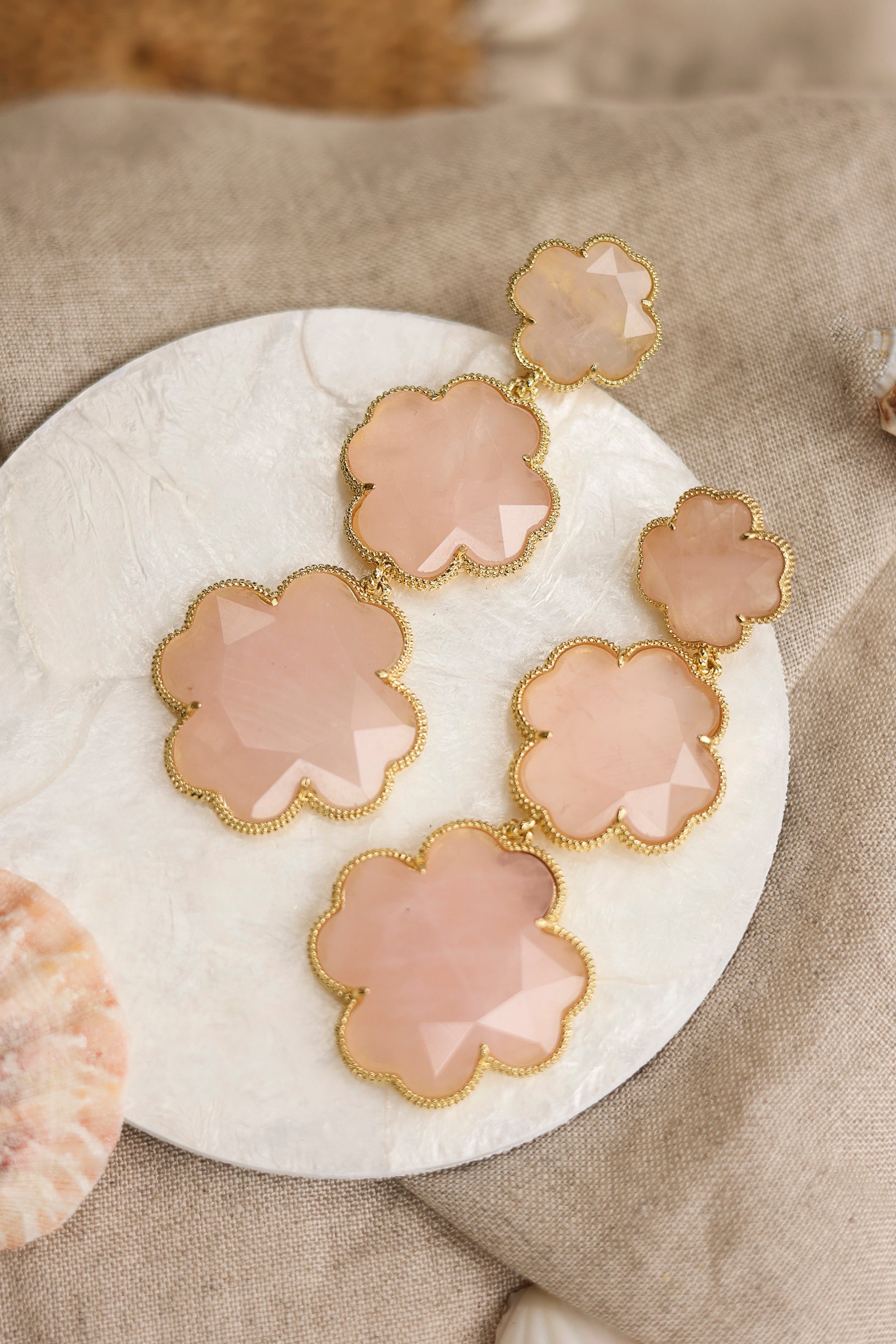 Boucles d'oreilles pendantes dorées Tharia quartz rose motif trèfles ornées de pierres naturelles - Bijou photographié dans un décor estival