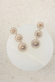 Boucles d'oreilles dorées Soledad pendantes soleils - Bijou photographié sur présentoir en marbre blanc