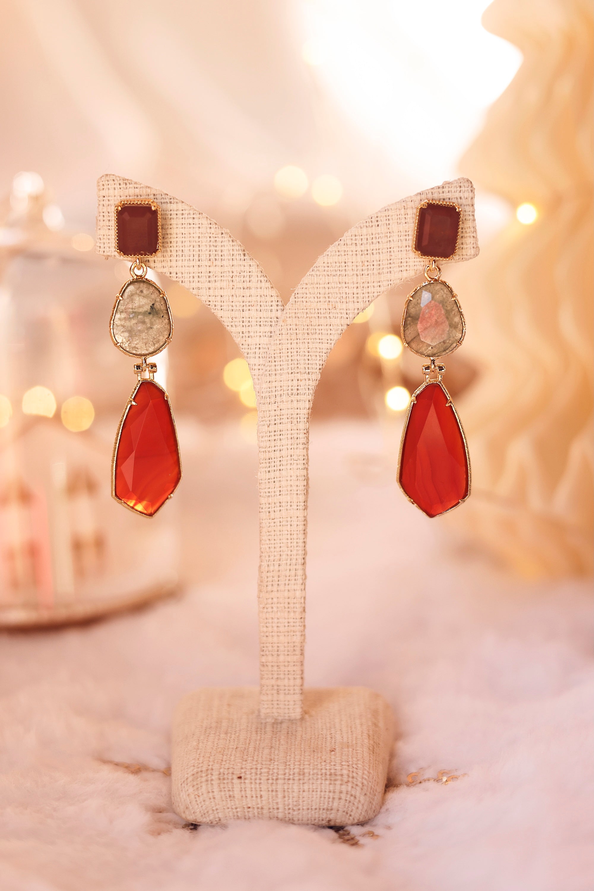Boucles d'oreilles pendantes dorées Varana rouge ornées de pierres naturelles - Bijou photographié sur un présentoir en lin