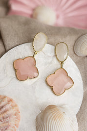 Boucles d'oreilles pendantes dorées Zephira quartz rose à motif trèfle ornées de pierres naturelles - Bijou photographié dans un décor estival