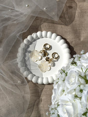 Boucles d'oreilles créoles Olya pendantes dorées avec auréole de perles en nacre et pendentifs fleurs - Bijou photographié dans une coupole blanche avec un voile de mariée et un bouquet de fleur