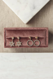 Boucles d'oreilles pendantes dorées Neije motif flocon de neige serties de zircons - Bijou photographié sur un présentoir en velours rose foncé