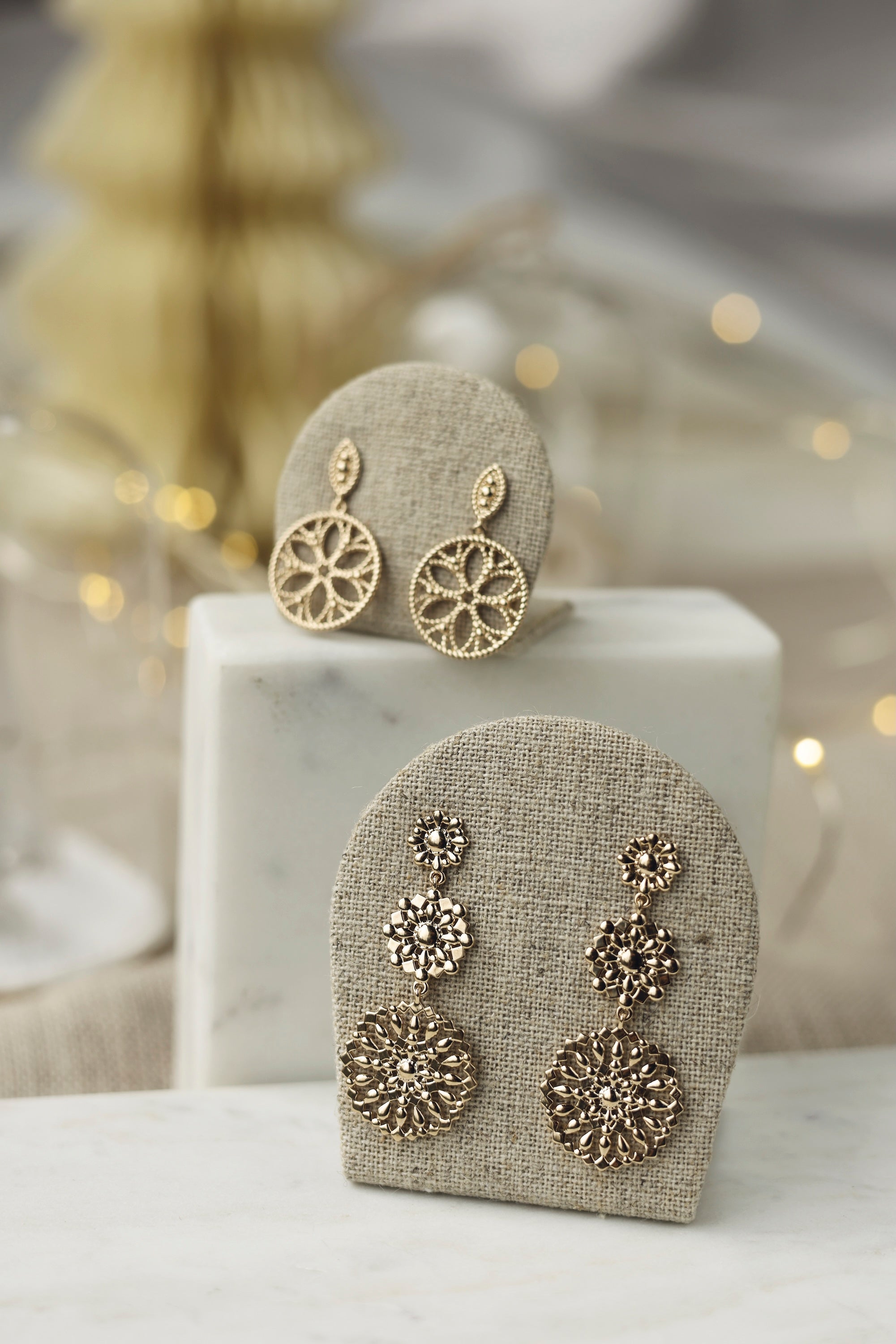 Boucles d'oreilles pendantes dorées Seviana motif mandala - Bijou photographié sur un présentoir en lin gris posé sur du marbre blanc avec des décorations de Noël en fond