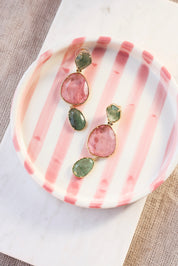 Boucles d'oreilles pendantes dorées Timy vert ornées de pierres naturelles - Bijou photographié dans un vide poche rayé rose et blanc