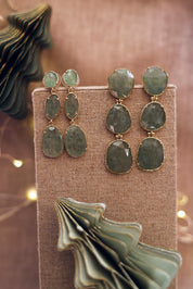 Boucles d'oreilles pendantes dorées Alissandra quartz fraise vert pierre naturelle - Bijou photographié sur un présentoir en lin gris