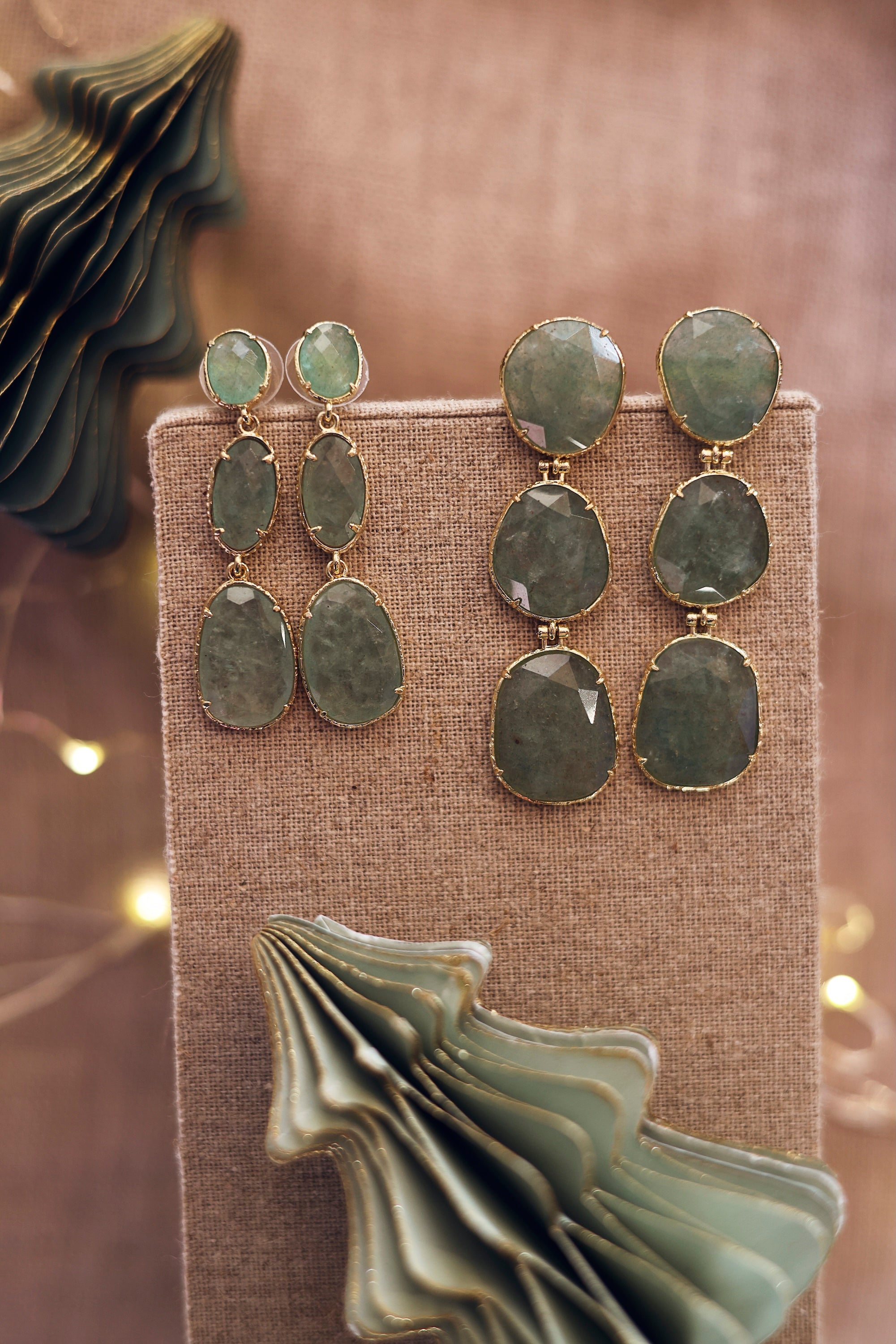 Boucles d'oreilles pendantes dorées Alissandra quartz fraise vert pierre naturelle - Bijou photographié sur un présentoir en lin gris