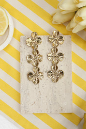 Boucles d'oreilles pendantes dorées Orianne ornées de fleurs - Bijou photographié dans un décor estival
