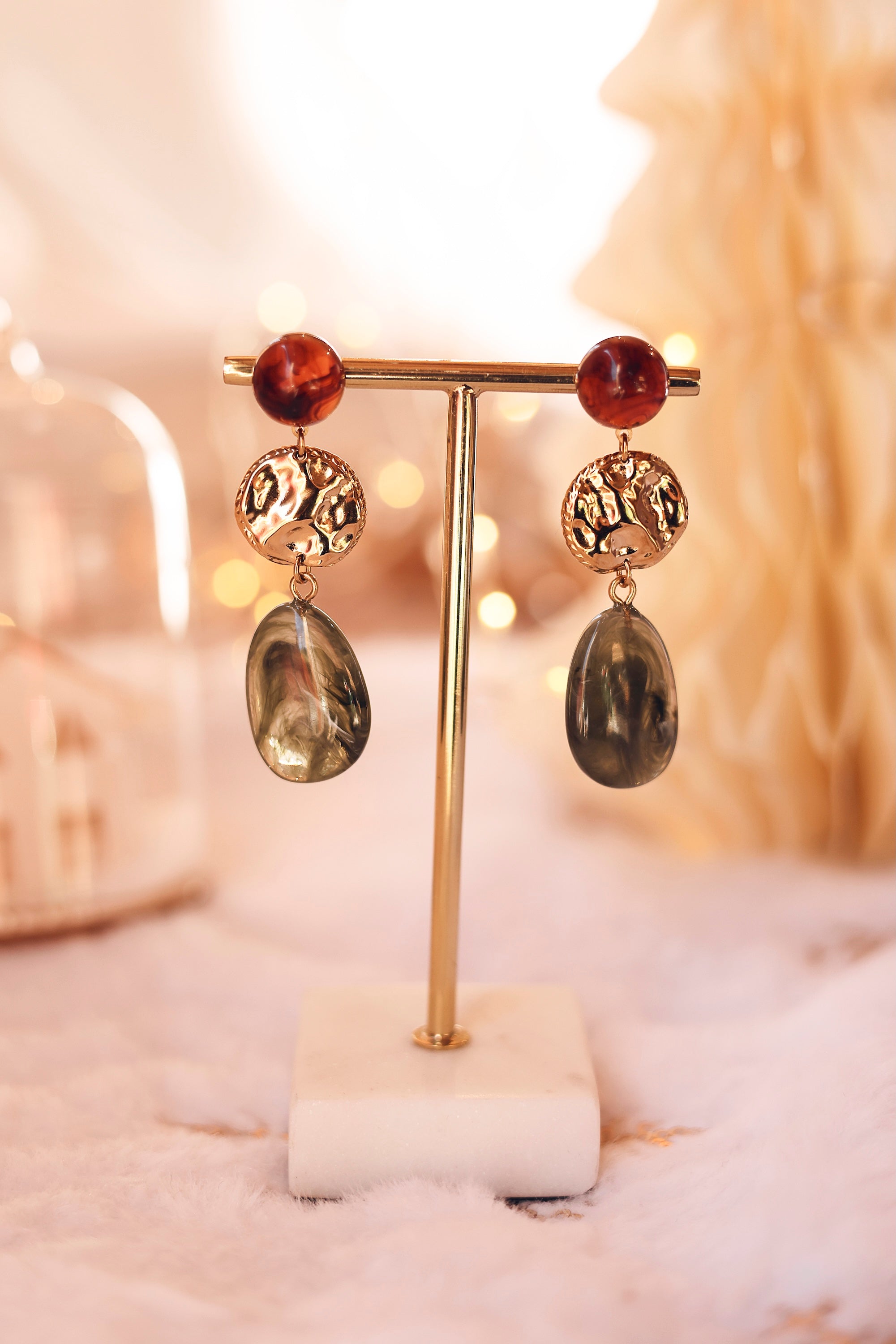 Boucles d'oreilles pendantes Sena dorées vertes et brunes - Bijou photographié sur un présentoir doré et marbre