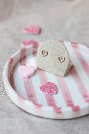 Boucles d'oreilles puces Alyssia dorées en forme de cœur ajouré ornées de zircons - Bijou photographié sur un présentoir en lin gris dans une ambiance saint valentin