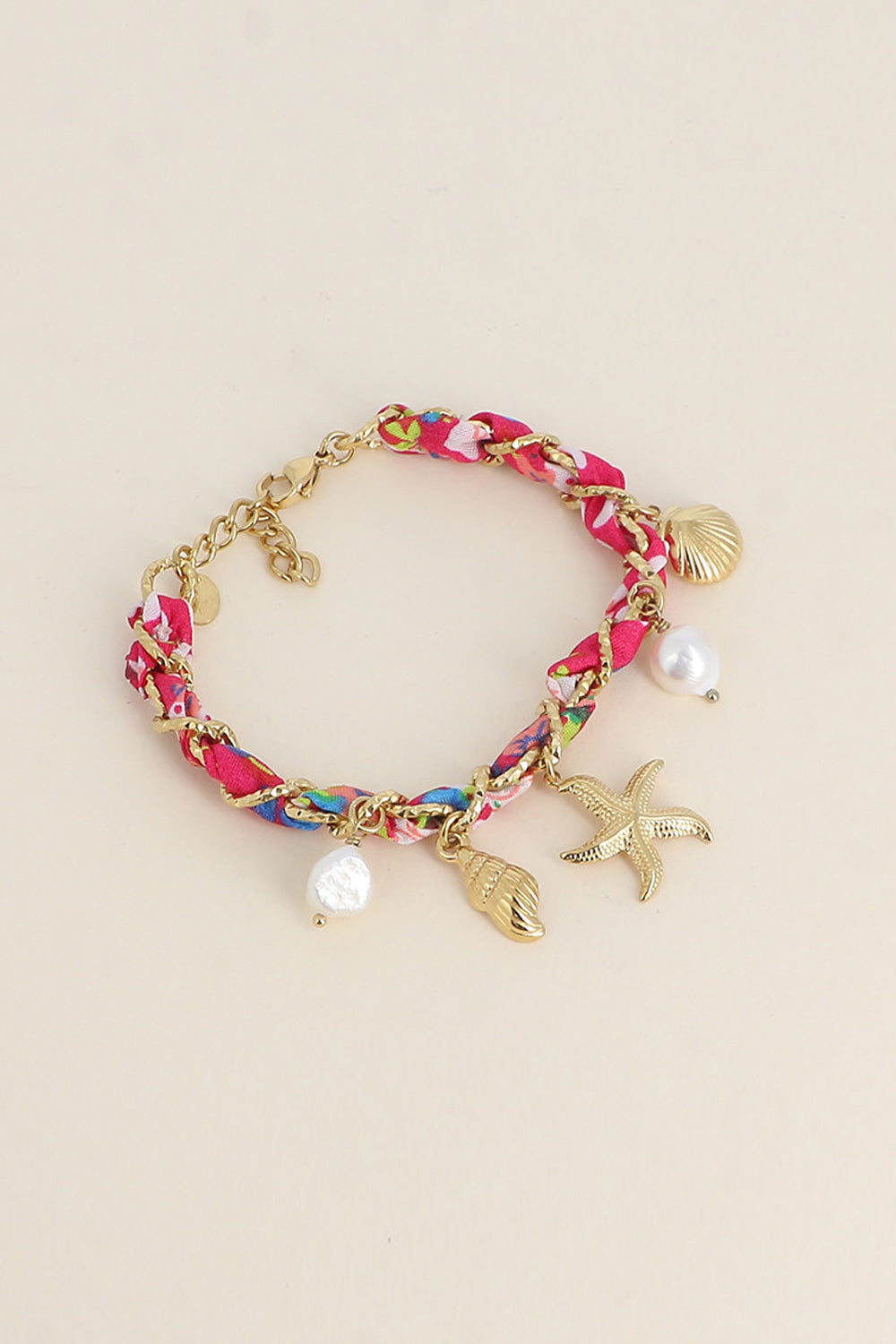 Bracelet doré Aminata fuchsia maille entrelacée avec tissu rose fuchsia pendentifs coquillages, étoile de mer et nacres - Bijou photographié sur fond beige
