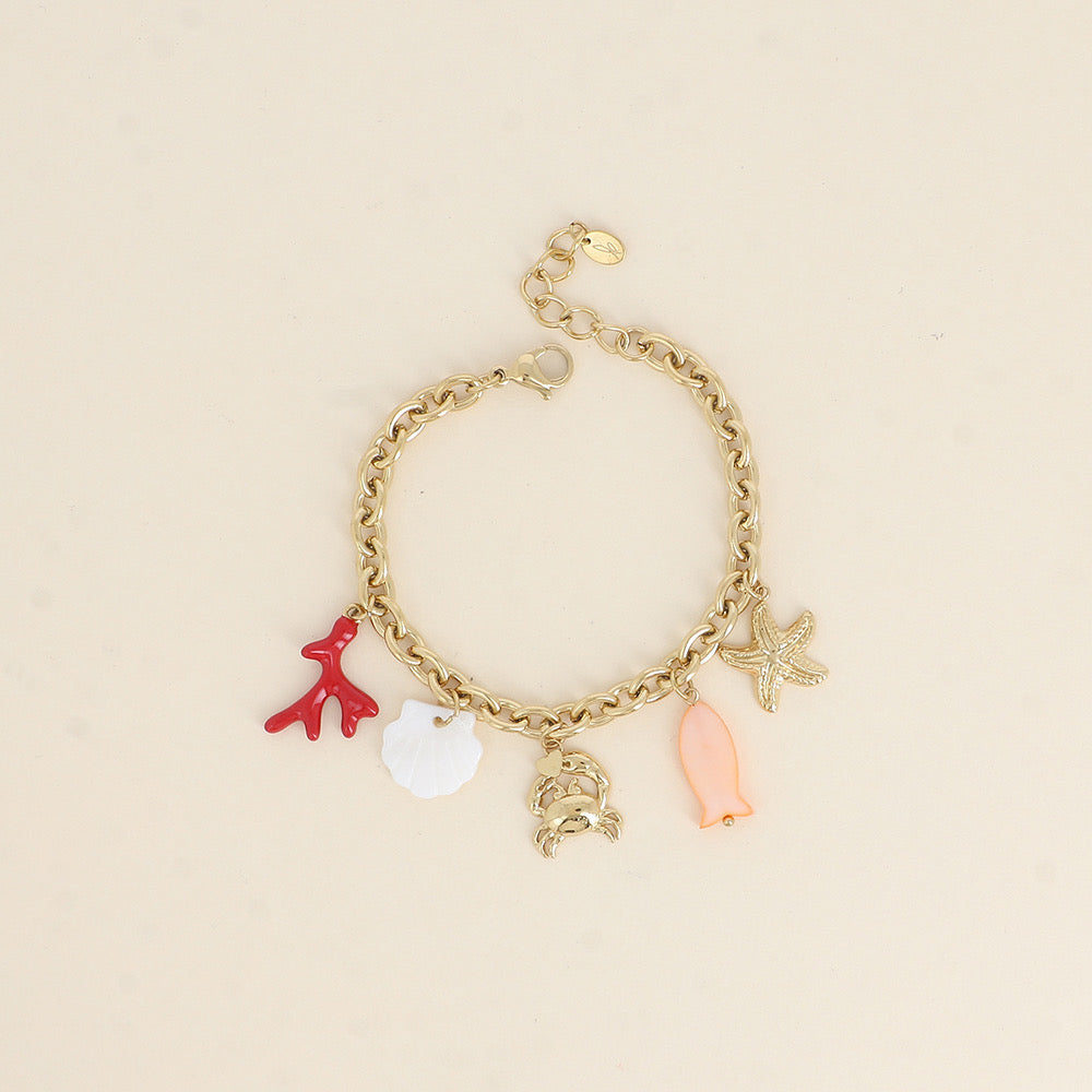 Bracelet maille doré Corail pendentifs coquillage en nacre, crabe qui porte un cœur, étoile de mer, poisson et corail - Bijou photographié sur fond beige