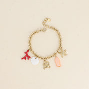 Bracelet maille doré Corail pendentifs coquillage en nacre, crabe qui porte un cœur, étoile de mer, poisson et corail - Bijou photographié sur fond beige