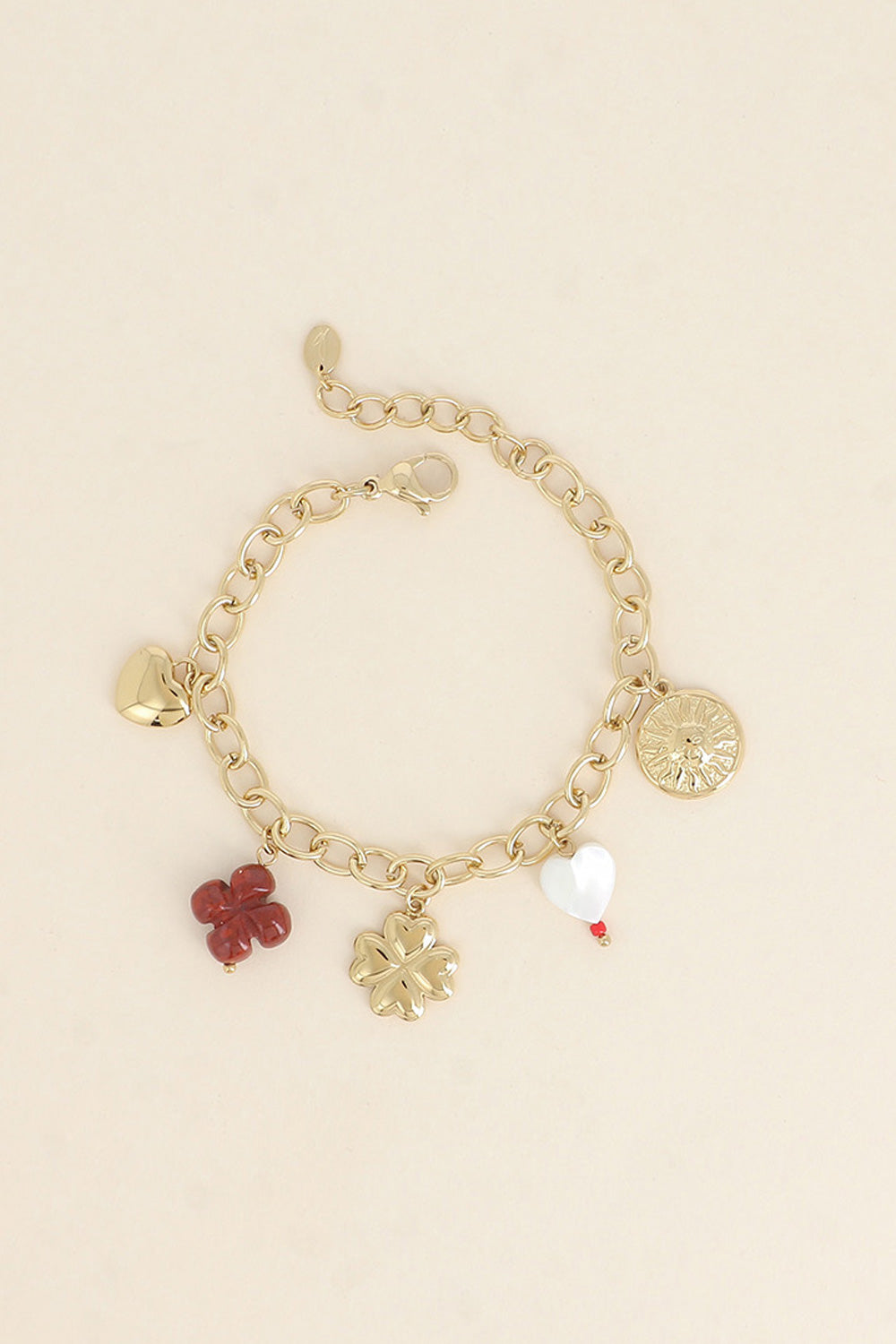Bracelet maille doré Sabeen pendentifs soleil, cœur, trèfle et nacre - Bijou photographié sur fond beige